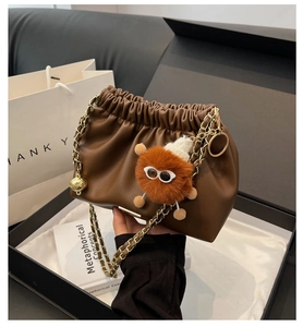 Detail of dark brown pleated bucket bag with gold chain strap in a premium gift box