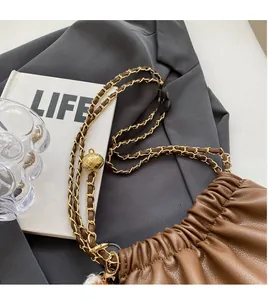Close-up of brown leather bucket bag with gold chain and sphere detail on grey fabric