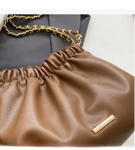 Detail of brown lychee texture leather bucket bag with gold metal trim and chain