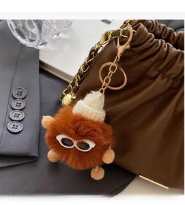 Close-up of fluffy brown keychain with sunglasses on a pleated leather handbag