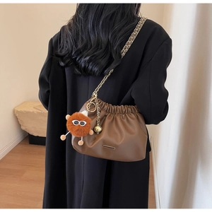 Close-up of brown pleated cloud bag with golden chain strap and plush monster charm
