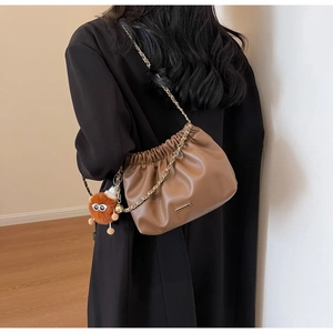 Detailed shot of brown pleated cloud bag featuring gold chain and orange fuzzy charm