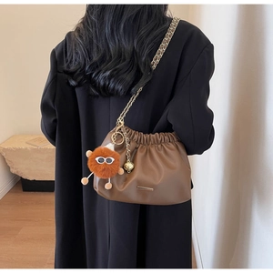 Close-up of brown pleated bucket bag with gold chain strap and plush pendant on model