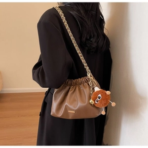 Detail of a brown pleated cloud bag with gold chain strap and cute monster plush charm