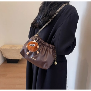 Detail of dark brown ruched bucket bag with gold chain strap and fuzzy monster charm