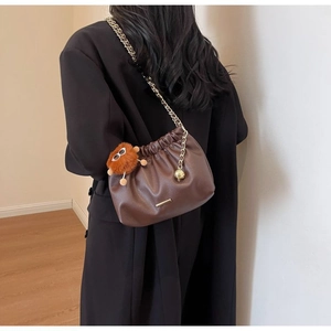 Detail of dark brown pleated cloud bag with gold chain and plush monster charm