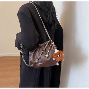 Detail of dark brown pleated bucket bag with gold chain strap and plush monster charm