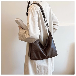 Detailed side view of brown crescent tote bag with glossy pleated leather and zipper