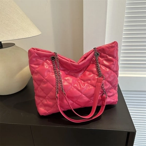 Bolso tote acolchado rosa fucsia con cadena plateada sobre superficie negra minimalista