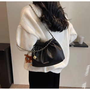 Detail view of black pleated bucket bag with gold chain strap and plush monster charm