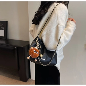 Detail of black pleated leather bucket bag with chain strap and plush monster charm