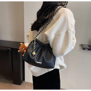Detail of black pleated bucket bag with gold chain strap and plush monster charm