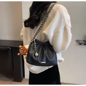 Detail of black pleated bucket bag with chain strap and cute plush charm on a model