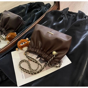 Close-up of deep brown litchi leather bucket bag with gold chain and plush charm