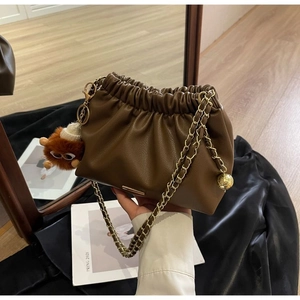 Detail of dark coffee ruched cloud bag with gold chain and plush monster charm