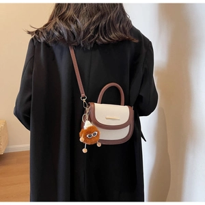 Detail of color-block saddle bag with plush charm and long strap on black blazer