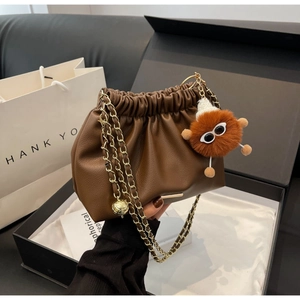 Detail of a brown pleated cloud bag with a gold chain and a fuzzy monster charm