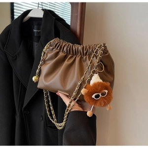 Detail of a brown ruched cloud bucket bag with gold chain and plush doll pendant
