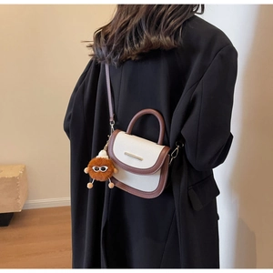 Detailed side view of two-tone saddle bag with cute brown plush monster pendant accessory