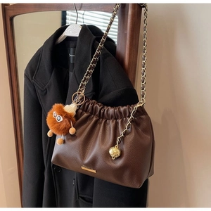 Detail of dark brown pebble leather bag with braided chain and fuzzy monster charm