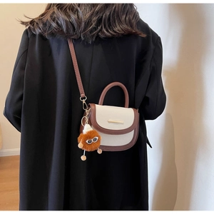 Detail view of contrast color saddle bag with a playful fluffy eyeball pendant charm