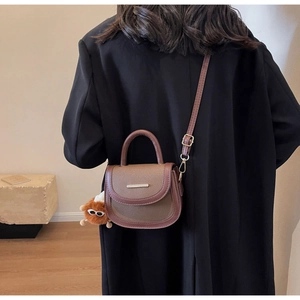 Detail of brown contrast saddle bag with plush monster charm and metal trim on black coat