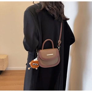 Detail view of a vintage brown leather saddle bag with an adjustable strap and plush charm
