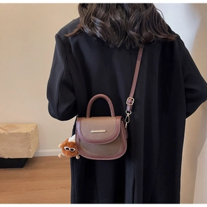Detail of color-block saddle bag with gold trim, top handle and plush monster charm