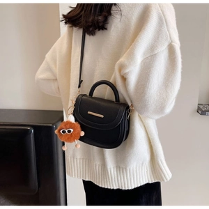 Detail of black crossbody bag with gold metal trim and orange fuzzy monster charm