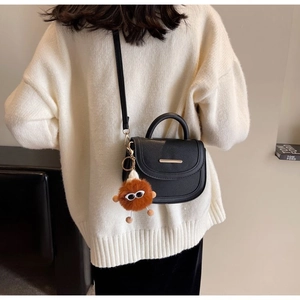 Detail of black pebbled leather saddle bag with gold hardware and plush monster charm
