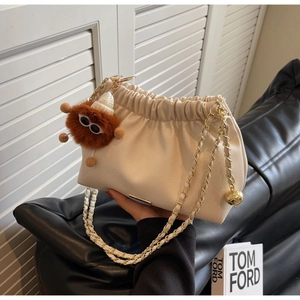 Detail of cream pleated bucket bag with gold chain strap and brown fluffy pompom charm