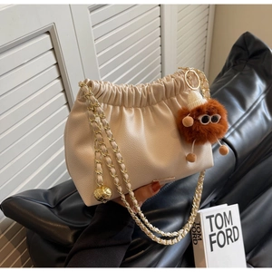 Detail of cream pleated bucket bag with gold chain strap and fuzzy monster charm