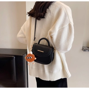 Detail of black semi-circle saddle bag with gold metal trim and brown plush charm