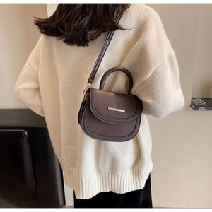 Detail of dark brown semi-circle saddle bag with gold metal trim and litchi texture