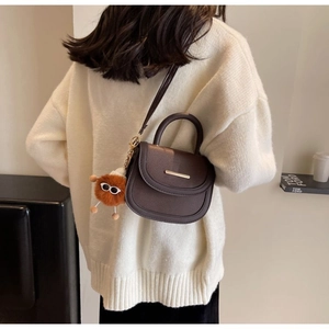 Close-up of brown pebbled leather saddle bag with gold metal hardware and plush charm