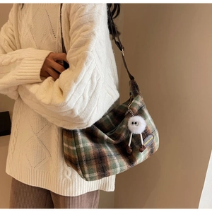 Detail of vintage plaid woolen tote bag with a cute plush monster charm on a white sweater