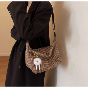 Detail of vintage brown plaid wool tote bag featuring a plush monster charm and leather tag