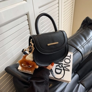 Minimalist black pebbled leather saddle bag with gold trim and brown plush charm