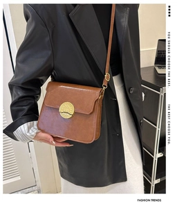 Detail of a brown leather crossbody bag with a spiral-textured gold circular metal buckle