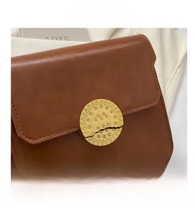 Close-up of vintage brown leather crossbody bag featuring a round golden metal clasp
