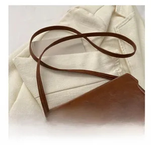 Detail of a brown leather shoulder bag with a textured wavy gold buckle on a beige blazer