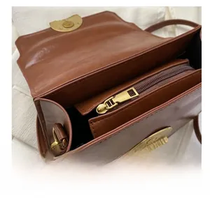 Macro detail of the smooth gold zipper and internal storage compartment of the brown bag
