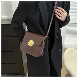 Detail of a dark brown crossbody bag with a textured gold round metallic buckle closure