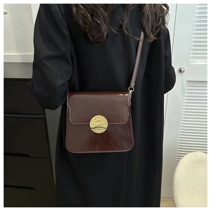 Close-up of a vintage dark brown leather crossbody bag with a gold embossed round buckle
