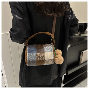 Detail of a plaid cylindrical pillow bag with a fluffy pom-pom and shoulder strap