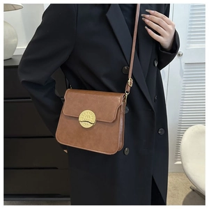 Detail of a brown leather shoulder bag featuring a textured gold round metal buckle