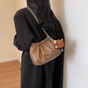Brown leather dumpling bag with gold chain strap and plush charm worn by model