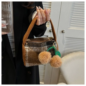Close-up of brown plaid wool pillow bag with corduroy handle and cherry pendant