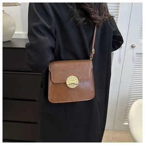 Detailed view of a vintage brown leather crossbody bag featuring a golden round buckle