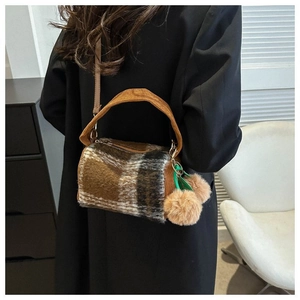 Detail showing retro plaid cylindrical bag with brown corduroy handles and plush pompom charm